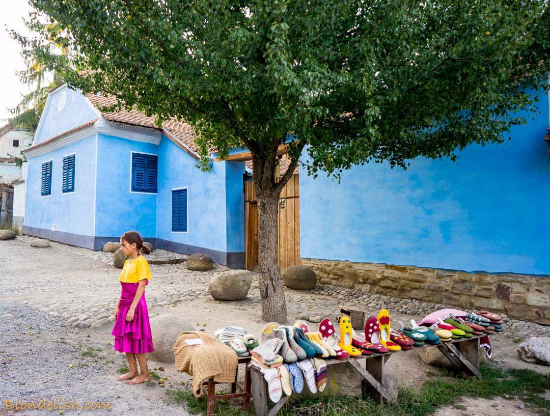 Little girl selling handmade things in front of a blue house, Transylvania, Viscri, Travel 